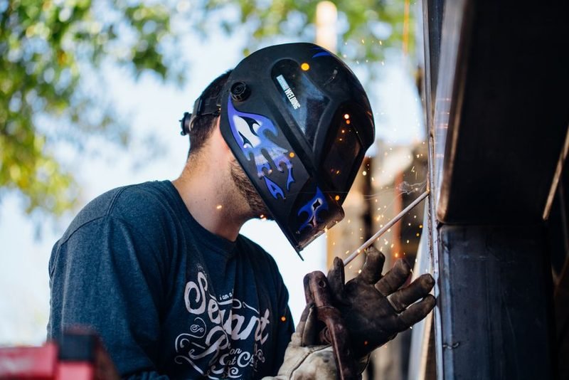 Welder running a bead outdoors, sparks coming off the joint.